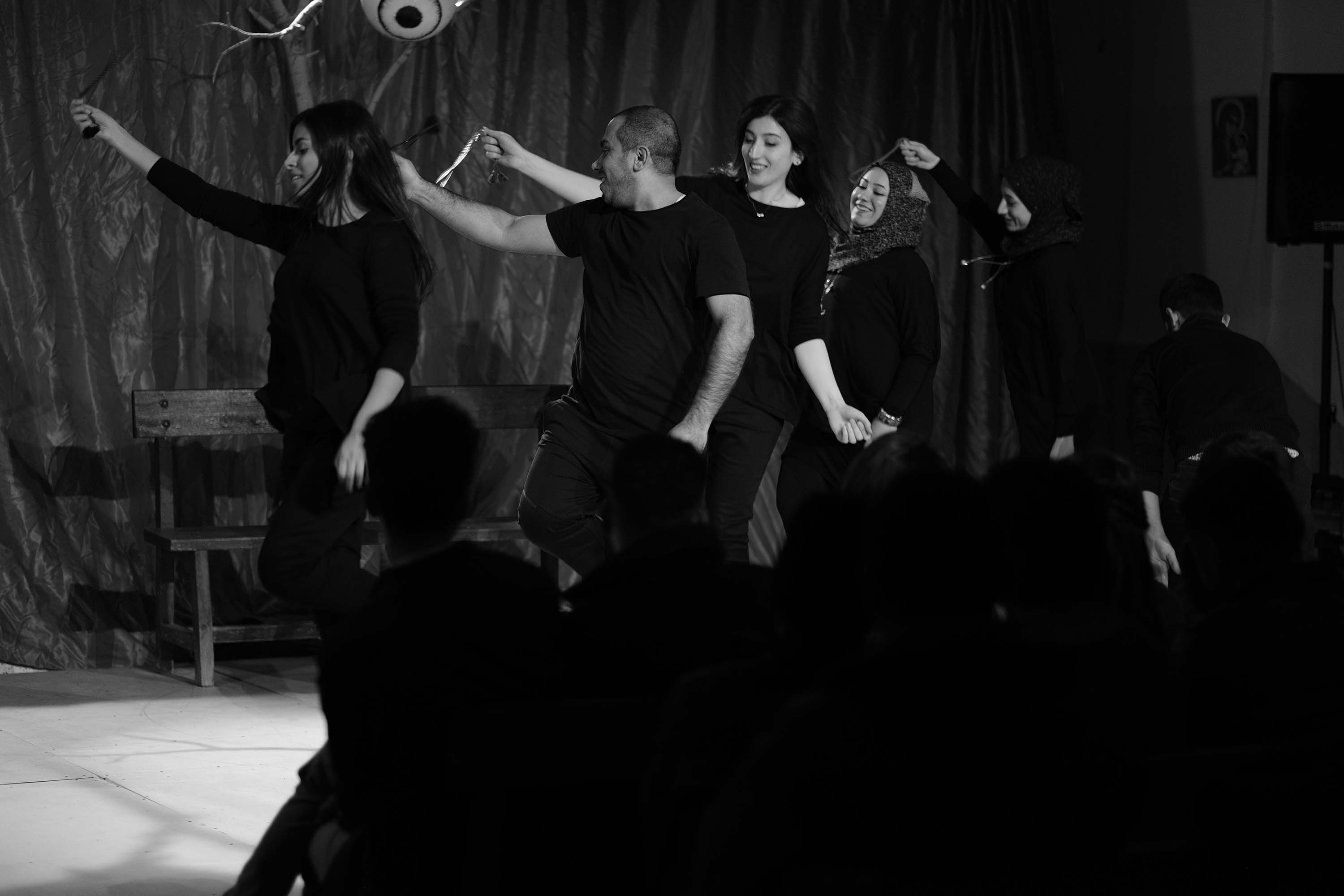  A series of black-and-whie images showing actors on a stage while moving around, holding hands and bowing in a line, standing in two lines across from each other holding ropes and in a single line dancing.