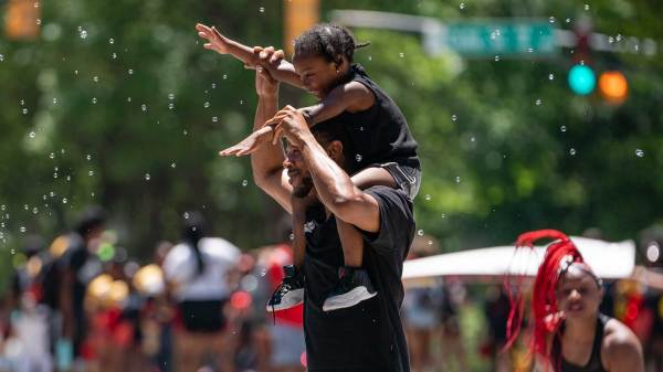 A Black man and a Blaack child enjoy bubbles blown by a spectator while marching in the Juneteenth Atlanta Black History parade.