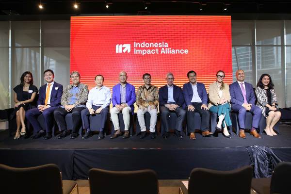 Group of people sitting in front of a large orange sign with the words "Indonesia Impact Alliance."