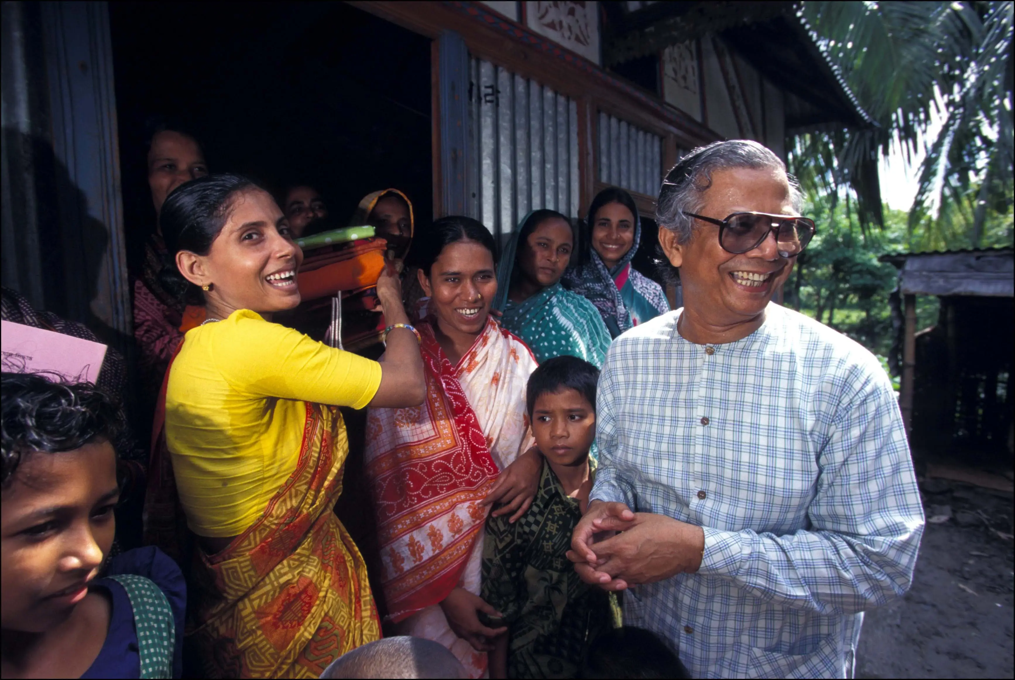 Muhammad Yunus laughs with Bangladeshi women and their families.